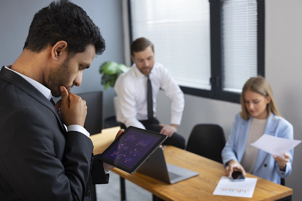 Homme consultant des graphiques sur une tablette devant ses collègues.